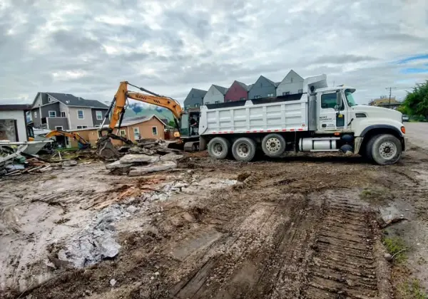 Excavator loading broken concrete debris into a Maxx Transfer dump truck at a townhome demolition site