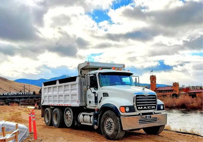 Maxx Transfer dump truck parked at a residential driveway pickup alongside a Paden Bros Landscaping trailer loaded with lumber
