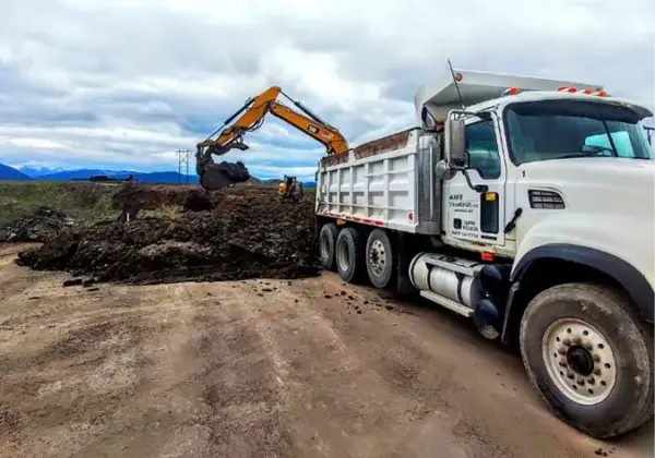 Dump truck parked on a street corner near a school with a front loader working in the background